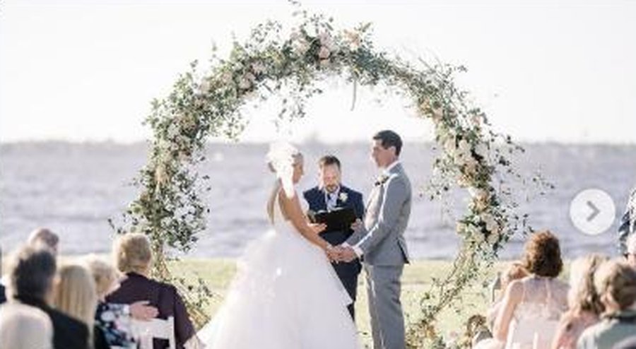 Outdoor waterfront wedding ceremony under a floral arch