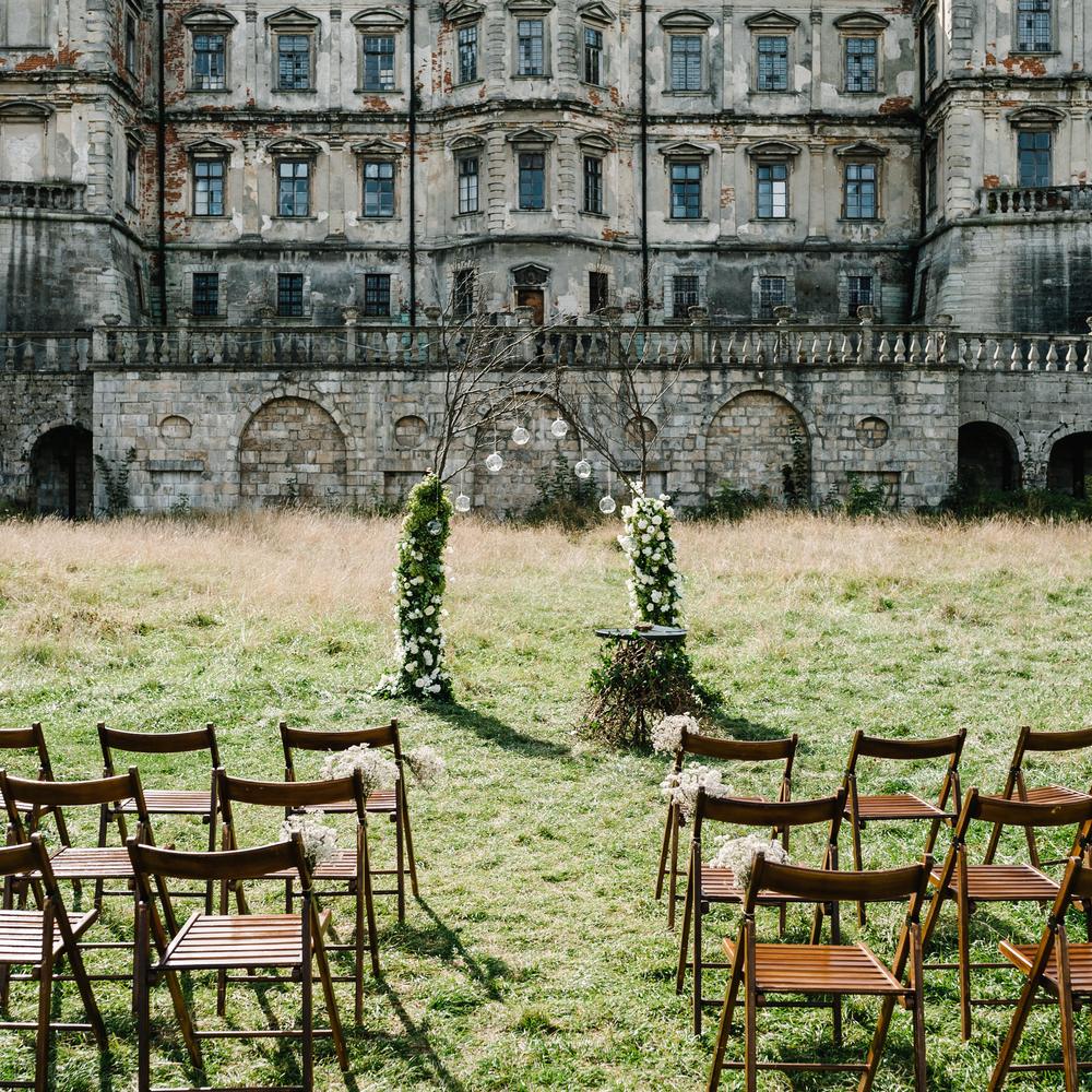 Outdoor wedding ceremony setup with wooden chairs and a floral arch